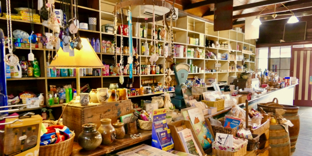  A wooden counter with and shelvescovered in crafts, pottery, antiques and books for sale under an open beamed cieling.