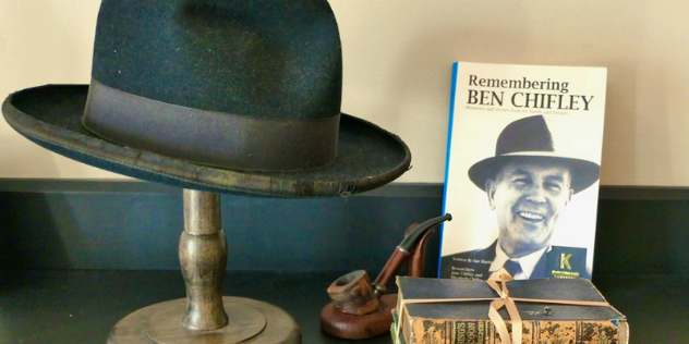 A well-worn black fedora hat on a stand next to a pipe, old books bound together, and a book titled Remembering Ben Chifley. 