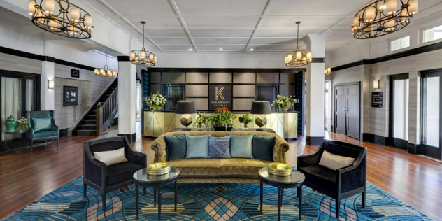  A hotel foyer with chandeliers, couches and front desk in blue, gold and brown, with art deco architecture.