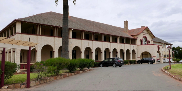  A tan stone and dark red trimmed hotel with a row of arches along the front, leading to the front entrance.