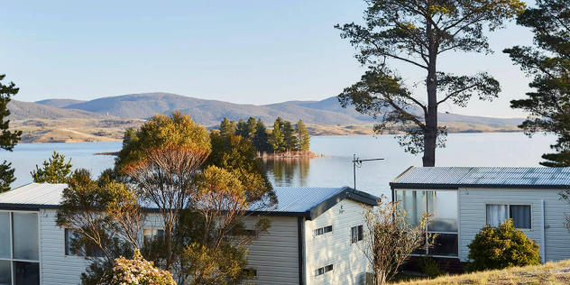 Holiday houses nestled among trees along a bay with a small island and large hills rising up from the opposite shore.