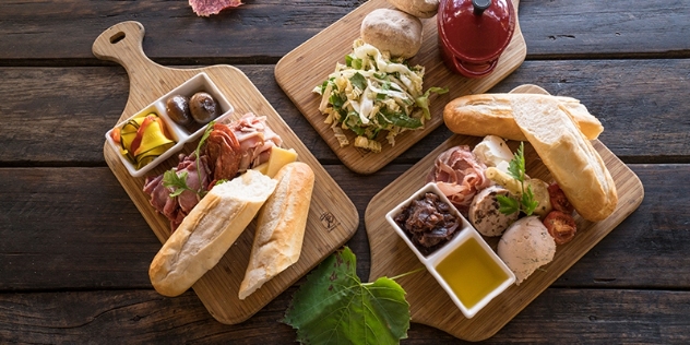 three wooden serving boards with tapas including bread, olive oil, salami and olives