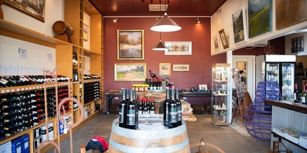 walls lined with horizontally displayed bottles of wine and wine barrels sit in the middle of the room also displaying bottles of wine