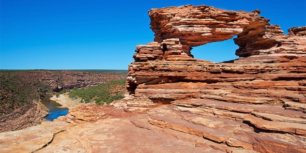 hilltop view of rock formation arch with arid landscape in the distance