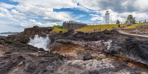 people on a viewing platform watch as water errupts from a hole in rthe rocks