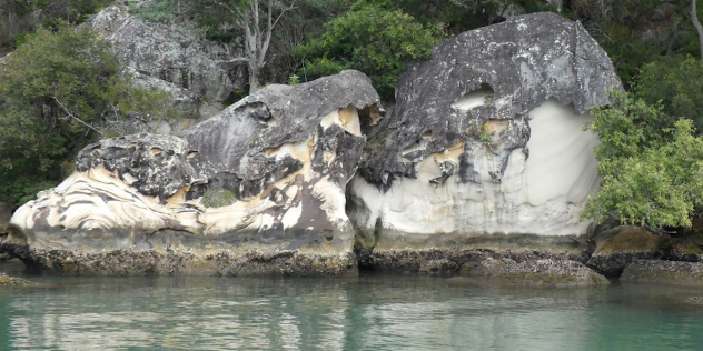 A shoreline with two rounded white and grey rocks framed by trees, indigenous art lines are faintly visible along the rocks.