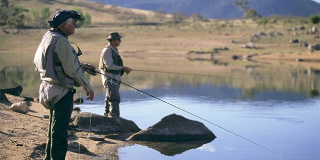 Two men in waders stand fishing at the edge of a lake