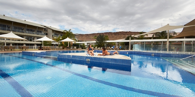 view of couple sunbathing on a raised platform in the centre of a swimming pool