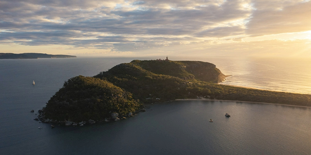  A treed peninsula shaped like an elephant's head with the trunk extending back to the shore, seen from a distance at sunset.