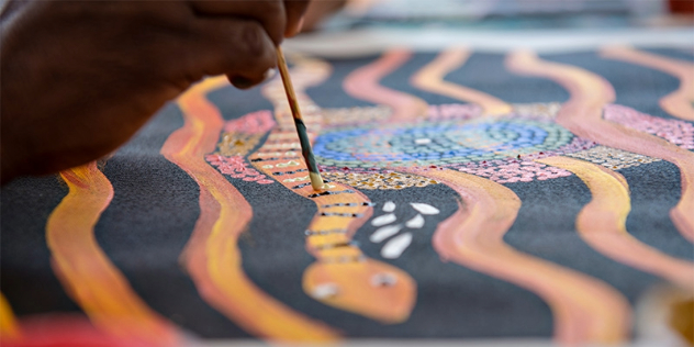 Close up of Aboriginal artwork featuring a colourful snake on a black background in progress