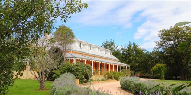 gravel drive flanked by lavender leads to pretty colonial cape cod style building with wide veranda