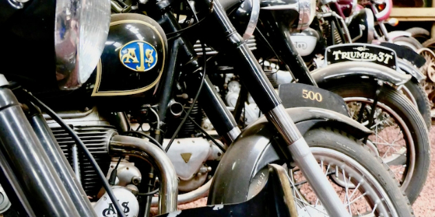 A close up of the front wheels of a row of vintage, black motorcycles. 