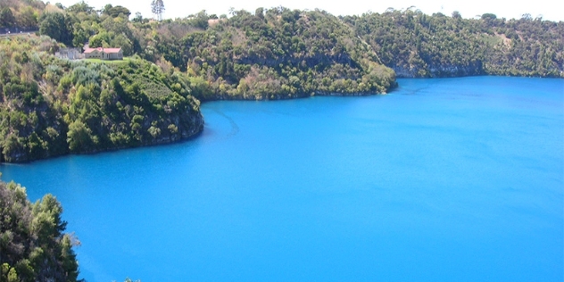 vivid mid blue water of the lake and tree covered peninsulas with a solitary building with a red tile roof