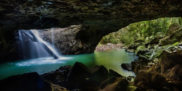 view from inside a basalt cave with a waterfall spilling through a hole in the roof into a turquoise pool