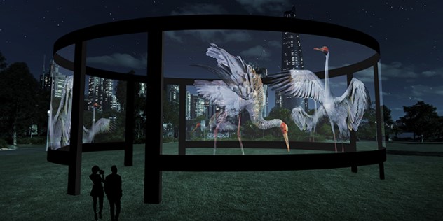  A round metal structure in a park at night, with projections of herons around the sides.