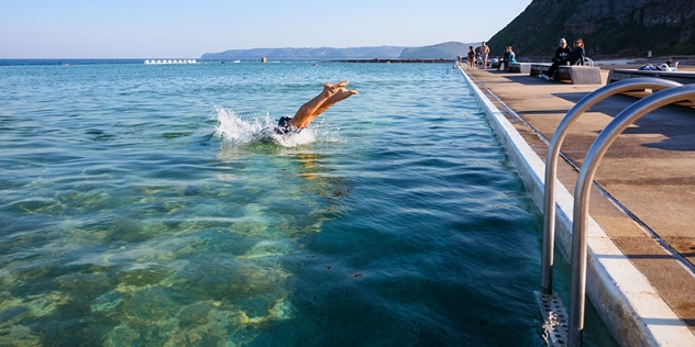 large infinity-style ocean pool with person diving in creating a splash