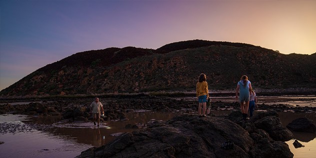 Parents and two children walking along the beach and overtop of rocks against a purple sunset, in Millstream-Chichester Park, Western Australia. 