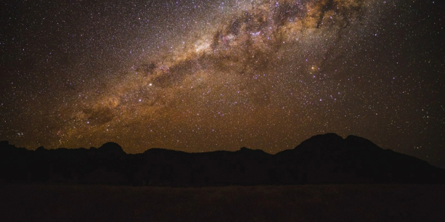  A galaxy of gold and violet stars silhouetting mountains below.