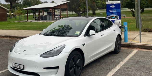 white testla charging at the NRMA Narrandera fast charger with park and undercover picnic area behind