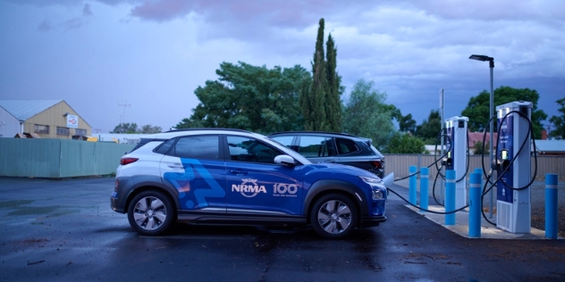 side view of blue and white NRMA electric vehicle plugged into an NRMA fast charger in a car park