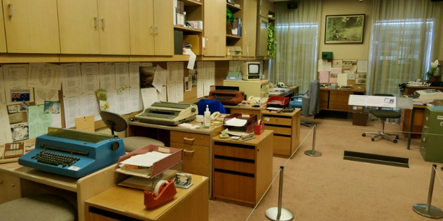  An an office last updated in the 70s or 80s, with rows of vintage typewriters and desks.