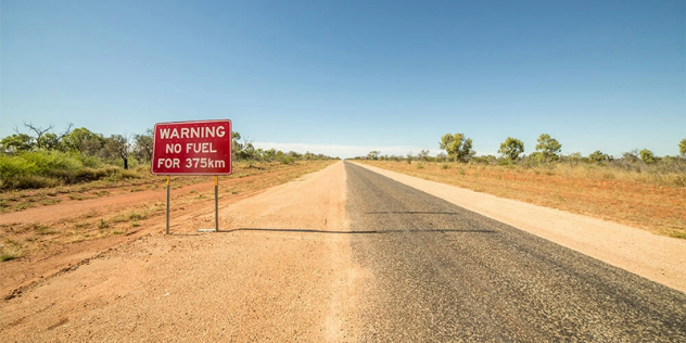 An empty, barely paved road in the outback with a sign saying warning no fuel for 375 kilometres. 