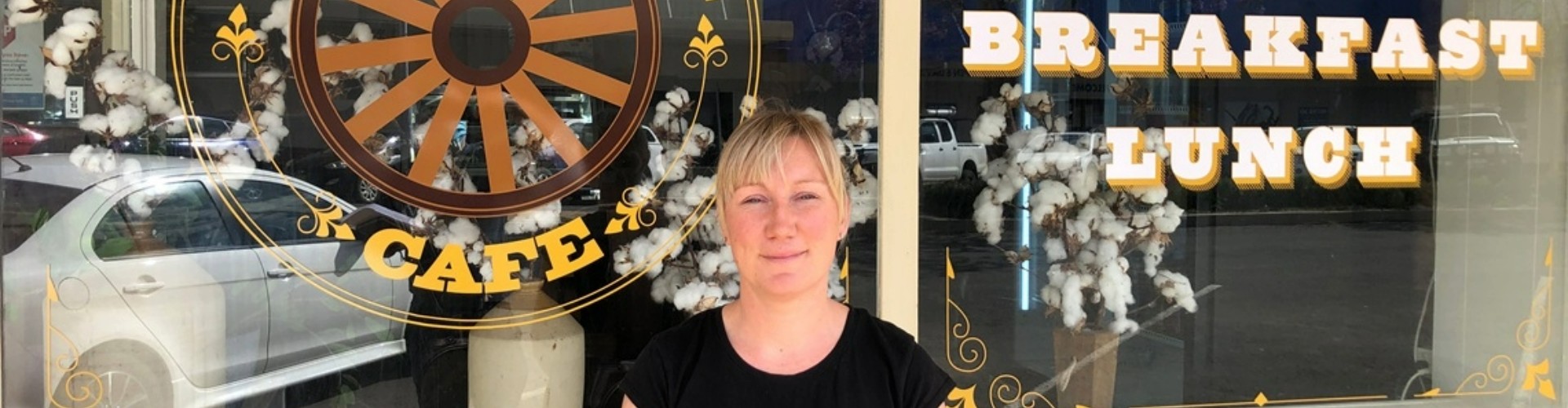 A woman standing beside a shop window with a round cafe logo printed on it.