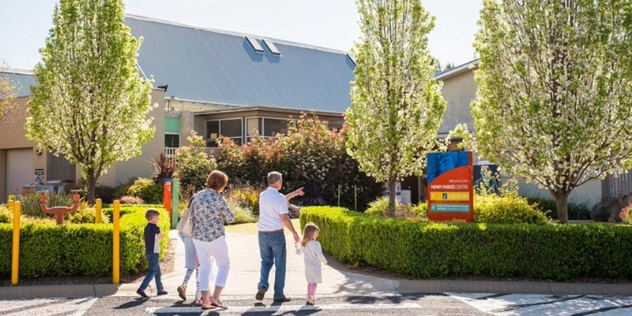 grandparents and three small children walk past entrance hedges towards a building with a sign saying Henry Parkes Centre