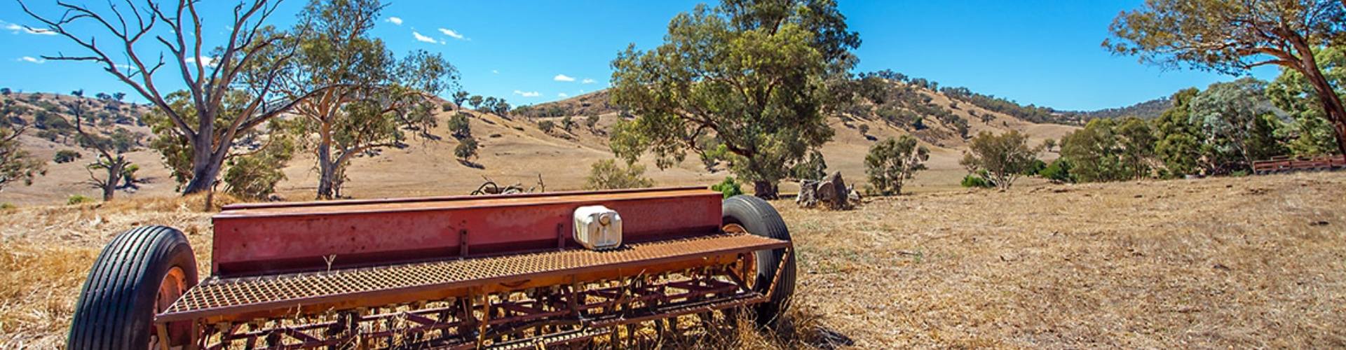 Parkes paddock NSW faded red farming equipment on dry grassland with hills and trees in the background