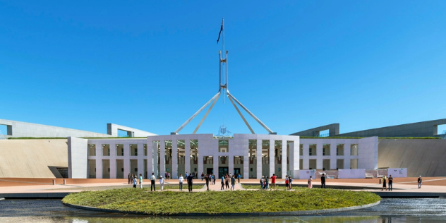  A white, minimalist interpretation of a columned building with a metal spire, with a round pool out front around a small grass island. 