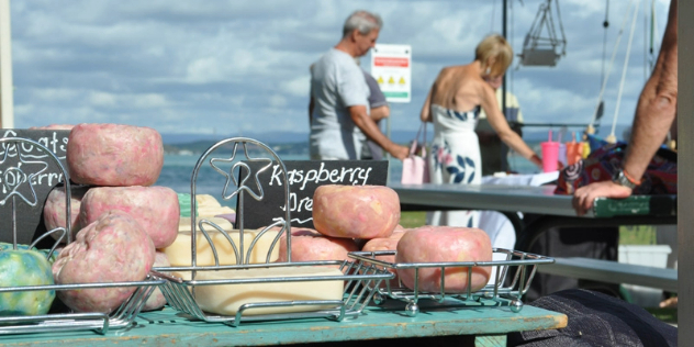  A pile of colourful soaps on a market bench along a sunny boardwalk, surrounded by shoppers. 