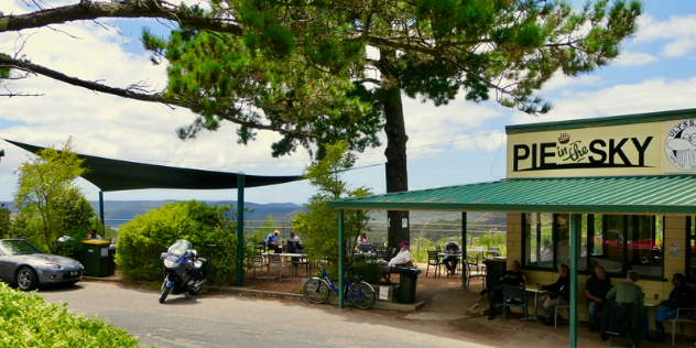  A flat topped cafe with Pie in the Sky written above a green awning, next to cafe tables and chairs overlooking a scenic valley