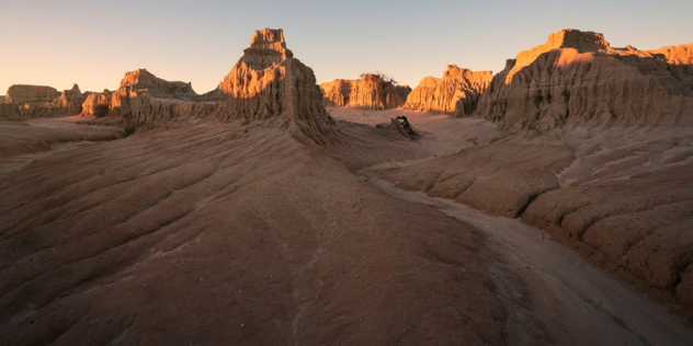 Golden sunset hits the tops of castle like sand formations rising out of a smooth rock landscape.