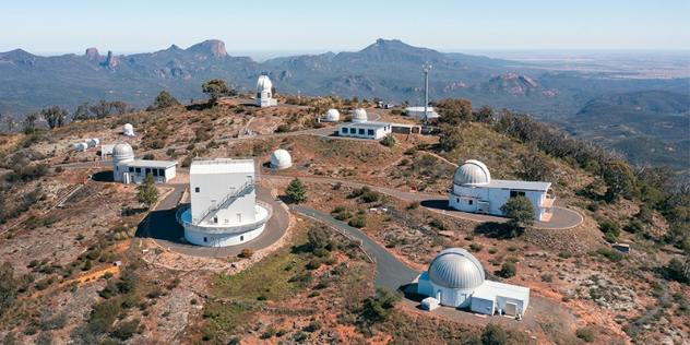  Multiple observatory domes at the top of a mountain in a vast canyon leading to plains in the distance.