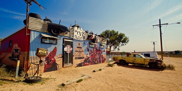 tin building painted with scenes from the mad max movies with a yellow car from the movies in front