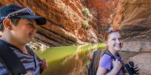 woman and boy smiling as they explore the gap in the rocky range with its water pools and orange rocks