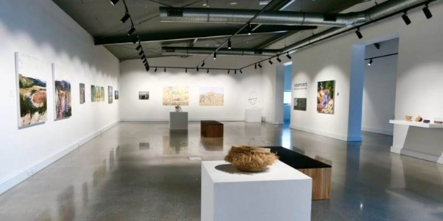  A gallery with white walls and concrete floors, with paintings on the walls and sculptures on pedestals.