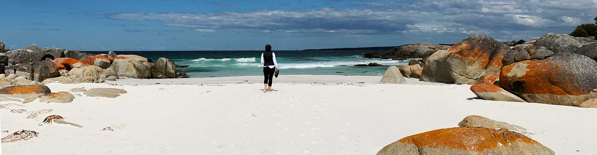 A woman walks on a beach surrounded by orange rocks