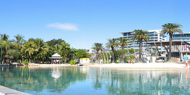  A man-made lagoon surrounded with thick palm trees, white sand beach, and restaurants and commercial buildings.