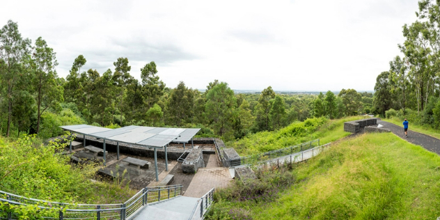  Stairs leading down to a picnic table area surrounded by lush grass and trees with a running path alongside it.