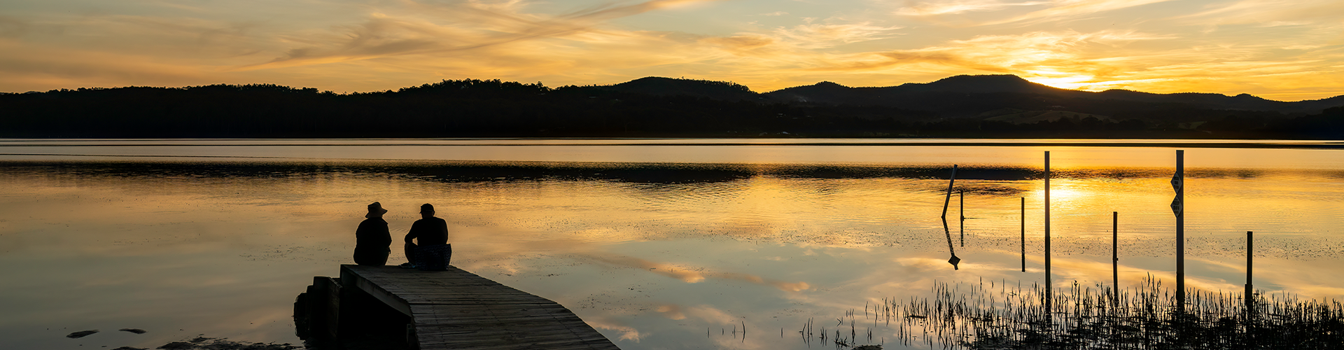 Two people watching the sunset over Merimbula Boardwalk