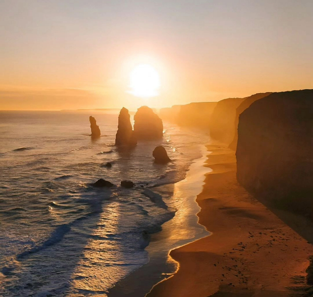 Four of the twelve apostle rock formations rising out of the sea along the beach silhouetted by a sunset.