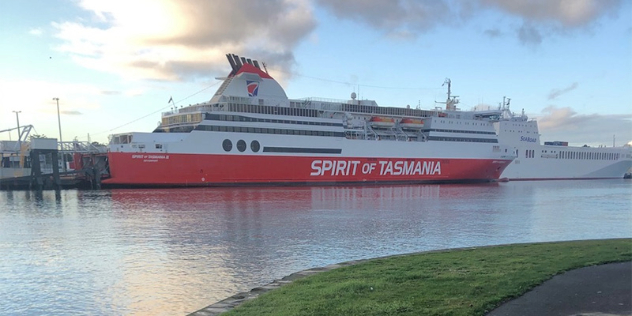 side view of the Spirit of Tasmania car ferry in port. The ship is painted white with the lower section painted red