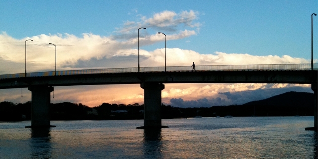 silhouette view of a bridge with person walking over it with sun behind