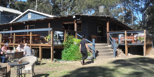 dark grey weatherboard building with deck and outdoor dining tables