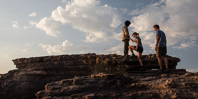 a woman being helped to the top of a rock by a man