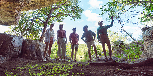 four people, shot from below, looking up into a cave