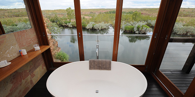 an indoor bathtub looking out onto open windows and the green lush view below