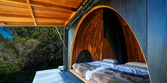 Two double beds on a treehouse platform, with a curved deck opening to trees and blue sky in Cod Bay, Tasmania.