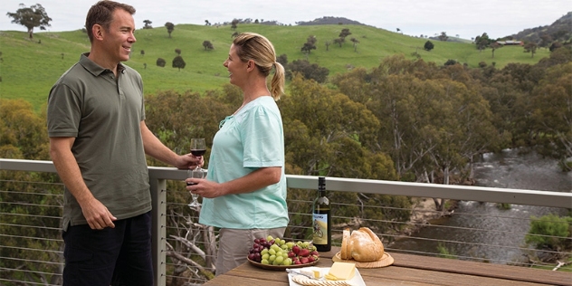 man and woman enjoying wine and a cheese platter on a deck overlooking a stream